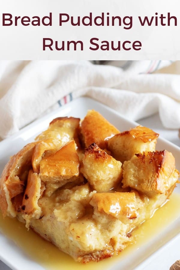 A large photo of the finished bread pudding, covered in rum sauce on white, square plate.