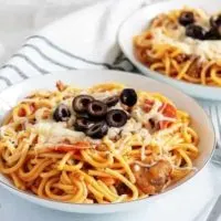 Two plates of pizza pasta next to striped linens and two forks.