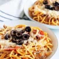 Two plates of Instant Pot Supreme Pizza Pasta topped with melted mozzarella cheese and black olives.