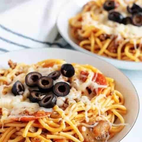 Two plates of Instant Pot Supreme Pizza Pasta topped with melted mozzarella cheese and black olives.