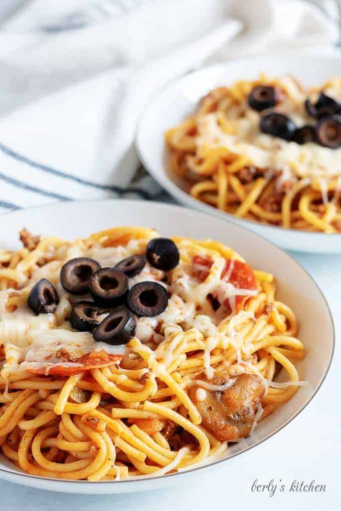 Two plates of Instant Pot Supreme Pizza Pasta topped with melted mozzarella cheese and black olives.