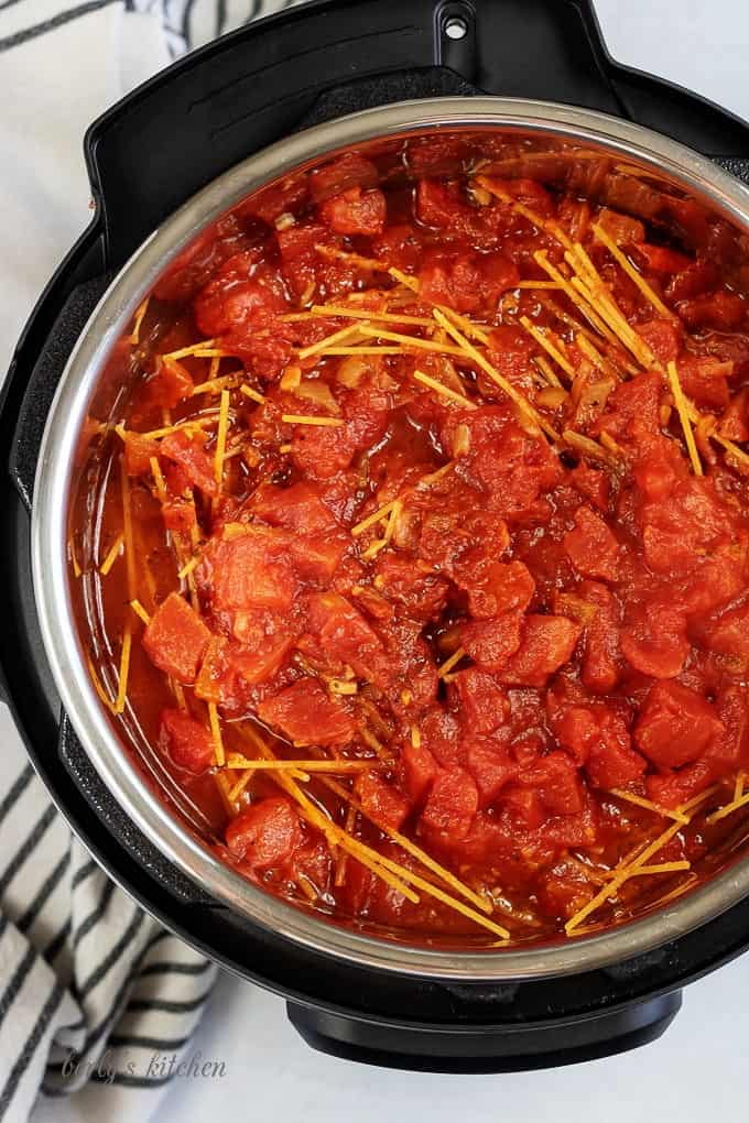 Top down view of spaghetti noodles topped with pasta sauce and tomatoes for supreme pizza pasta.