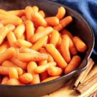 Maple Glazed Carrots in a cast iron skillet next to a blue linen.
