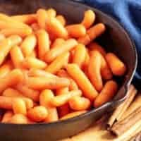 Maple glazed carrots in a cast iron skillet next to a blue linen.