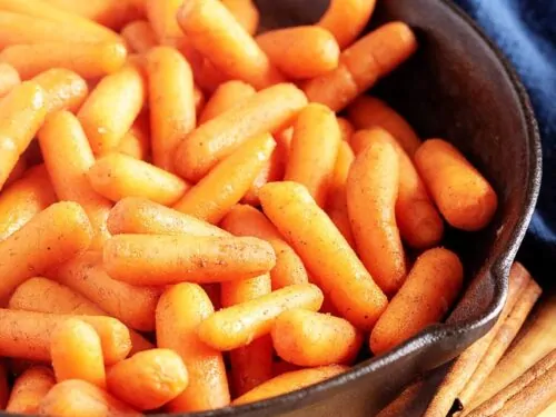 Maple glazed carrots in a cast iron skillet next to a blue linen.