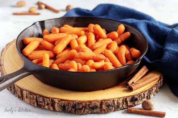 Maple Glazed Carrots in a cast iron skillet on a wood board. 