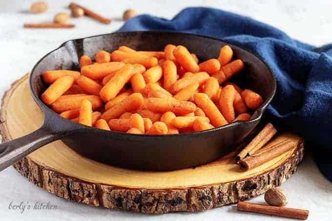 Maple glazed carrots in a cast iron skillet on a wood board.