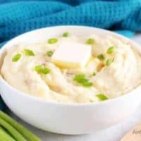 An angled picture of the mashed red potatoes in a serving bowl topped with butter and green onions.
