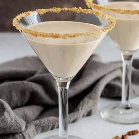Two pecan pie martinis in glasses rimmed with brown sugar, maple syrup, and pecans.
