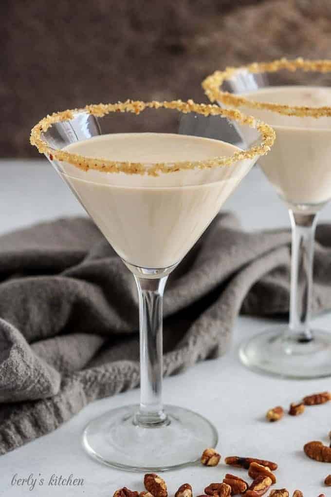 Two pecan pie martinis in glasses rimmed with brown sugar, maple syrup, and pecans.