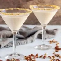 Two pecan pie martinis in martini glasses, rimmed with brown sugar and pecans.