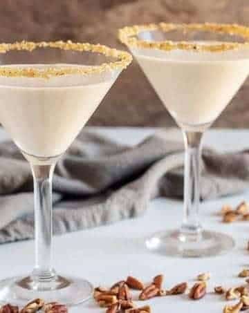 Two pecan pie martinis in martini glasses, rimmed with brown sugar and pecans.
