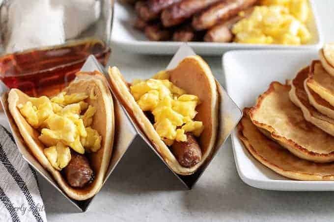 Two breakfast tacos in holders loaded with eggs, sausage, and syrup.