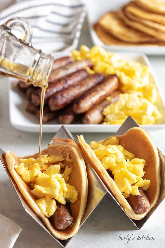 The tacos have been built with sausage and eggs, and topped with maple syrup.