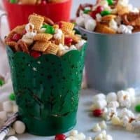 Christmas Chex Mix in festive tins with popcorn and candy scattered around.