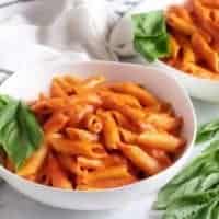 Two bowls of penne with vodka sauce and basil.