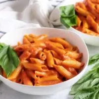 Two bowls of penne with vodka sauce and basil.