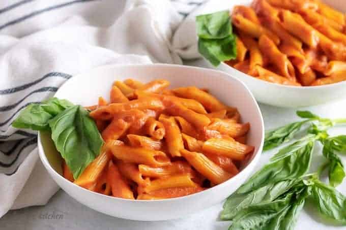 Two bowls of penne with vodka sauce and basil.