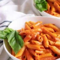 Two white bowls filled with penne with vodka sauce and fresh basil.