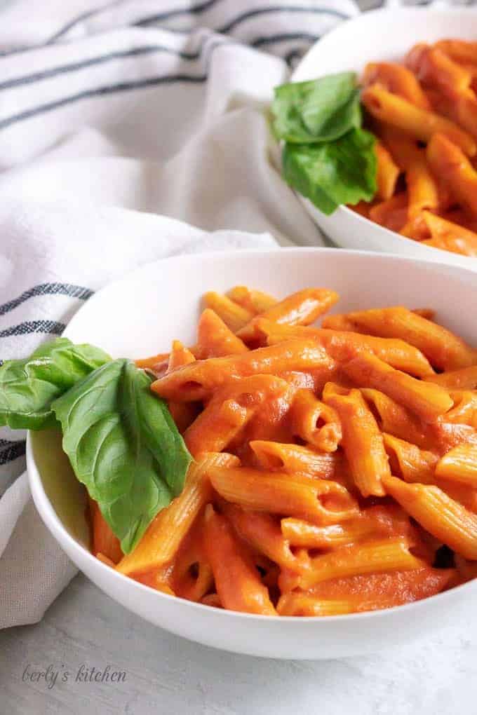 Two white bowls filled with penne with vodka sauce and fresh basil.