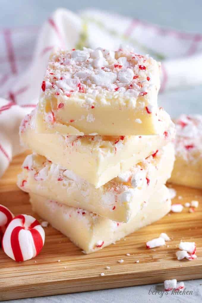 Four pieces of peppermint fudge stacked on a cutting board for presentation.