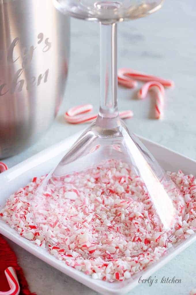 A martini glass, rimmed with syrup, being dipped into crushed candy canes.