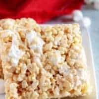 Two large rice krispie treats on a white plate next to a red napkin.