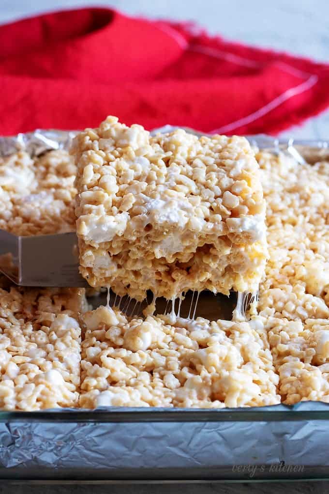 Pan of cut rice krispie treats with one being removed with a spatula.