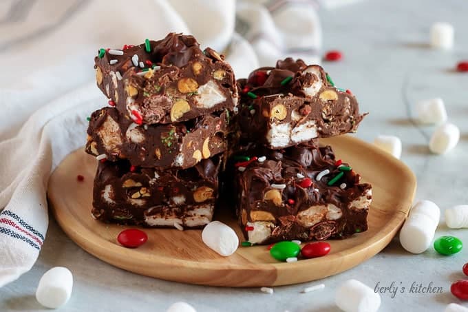 The rocky road fudge stacked on a wooden plate accented with candy.