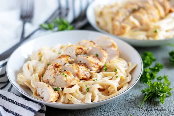 A bowl with fettuccine covered in alfredo sauce and topped with chicken.