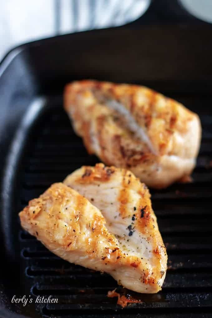 Two pieces of chicken breast being cooked on a hot griddle.