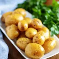 The finished baby potatoes, with fresh herbs, on a rectangular plate.