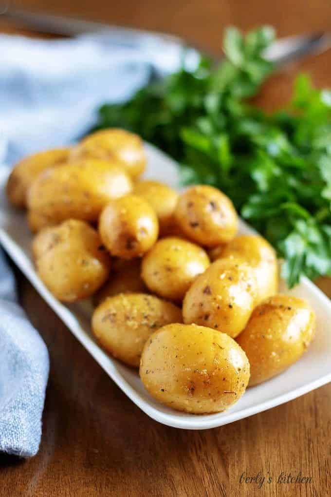 The finished baby potatoes, with fresh herbs, on a rectangular plate.