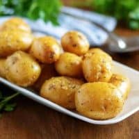 The baby potatoes, covered in butter, on a serving white plate.