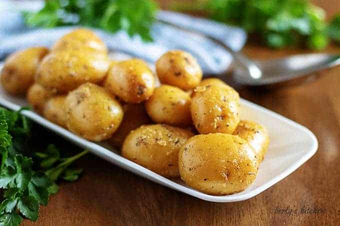 The baby potatoes, covered in butter, on a serving white plate.