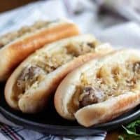 Three beer brats, in buns, topped with sauerkraut and onions.