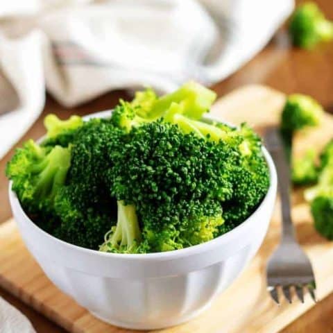 A picture of the steamed broccoli in a bowl on a cutting board.