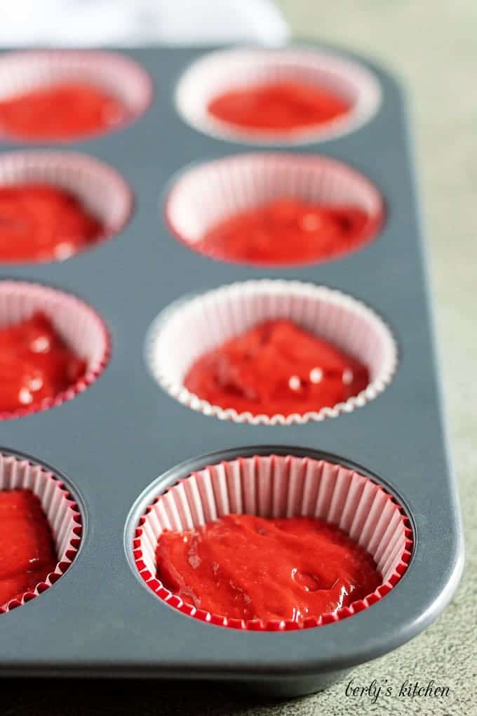 The cupcake liners in the pan, half filled with red velvet batter.