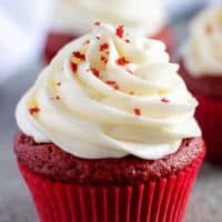 A red velvet cupcake, with cream cheese frosting, in a red liner.
