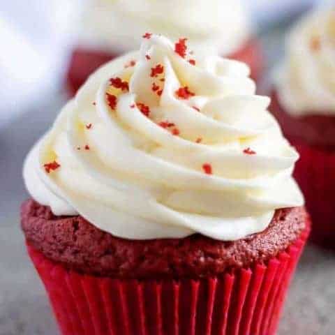 A red velvet cupcake, with cream cheese frosting, in a red liner.
