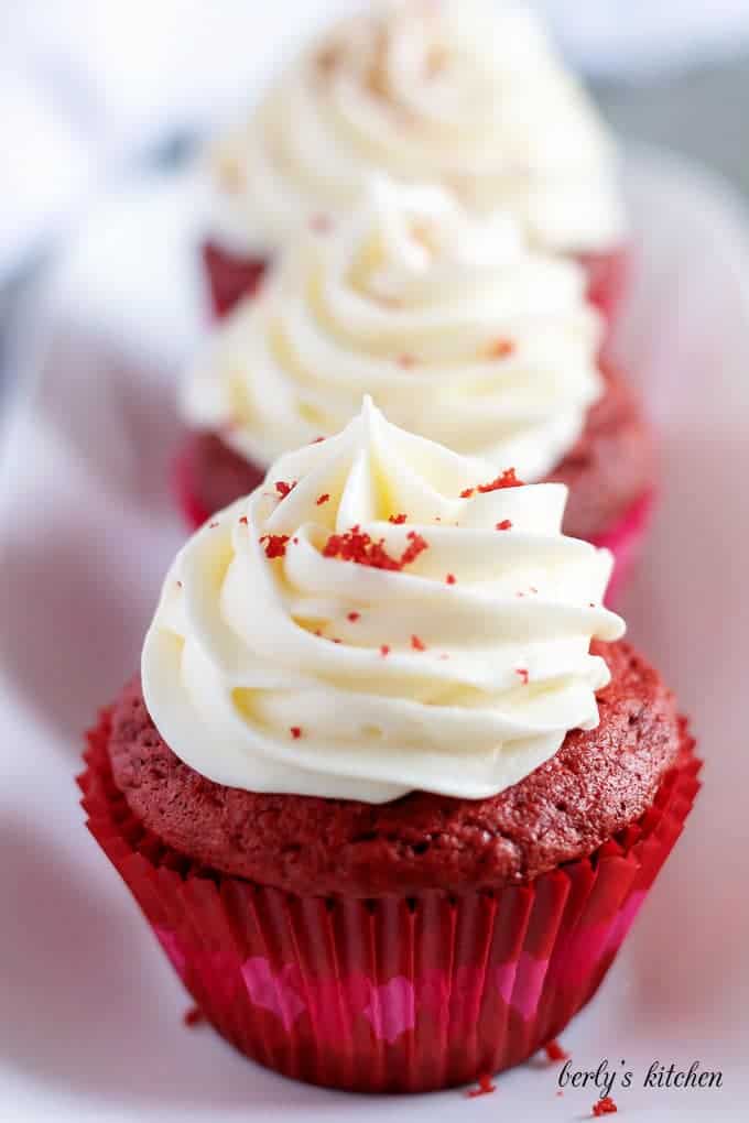 Three red velvet cupcakes, in a row, on a rectangular serving dish.