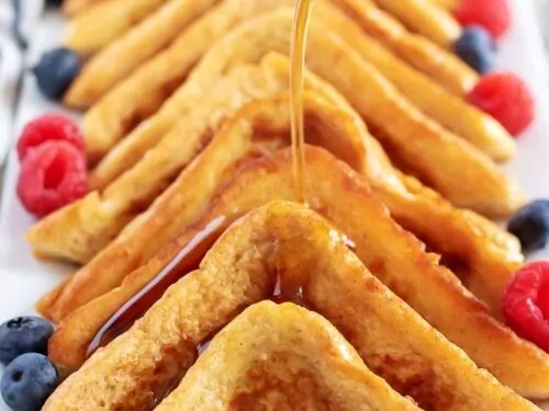 Cinnamon french toast slices lined on a white dish with syrup.