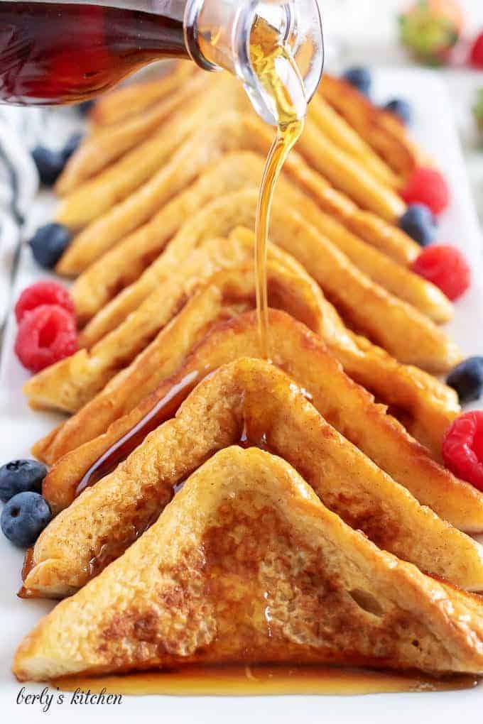 French toast slices lined on a white dish with drizzled with syrup.