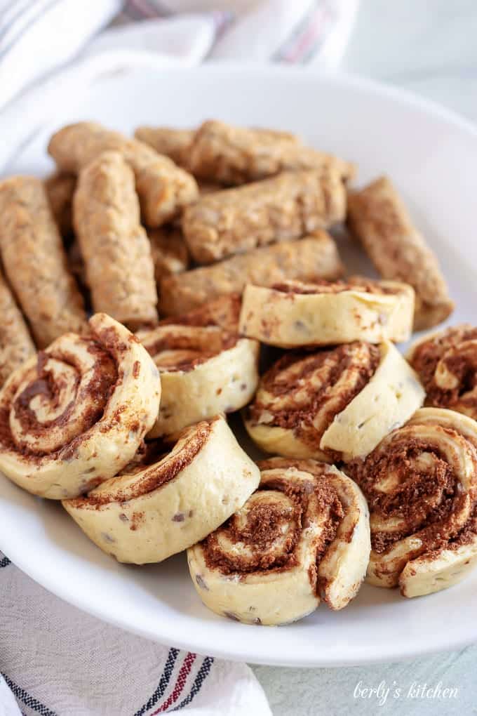 Uncooked sausage and raw cinnamon rolls prepped on a plate for assembly.