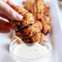 A picture of a sausage roll being dipped in warm icing.