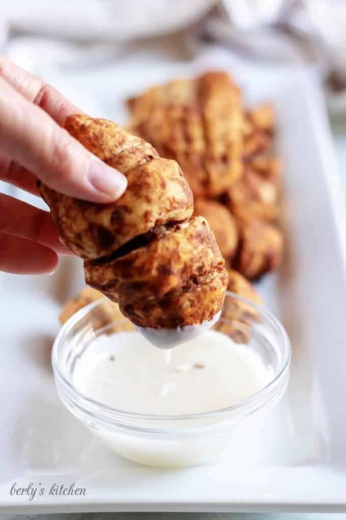 A picture of a sausage roll being dipped in warm icing.