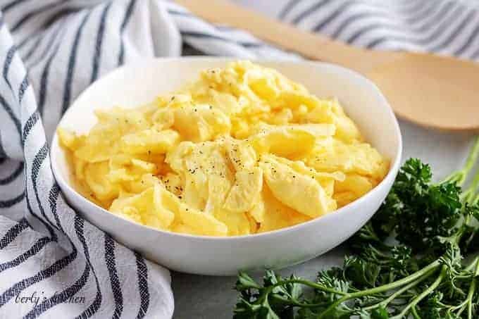 A bowl of fluffy scrambled eggs, sprinkled with ground black pepper.