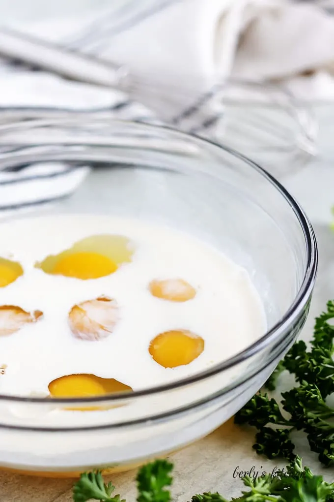 A large glass mixing bowl with the eggs, cream, and sea salt.