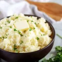 Final shot of the garlic mashed potatoes in a bowl, with butter and parsley.