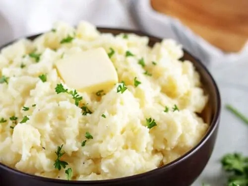 Final shot of the garlic mashed potatoes in a bowl, with butter and parsley.